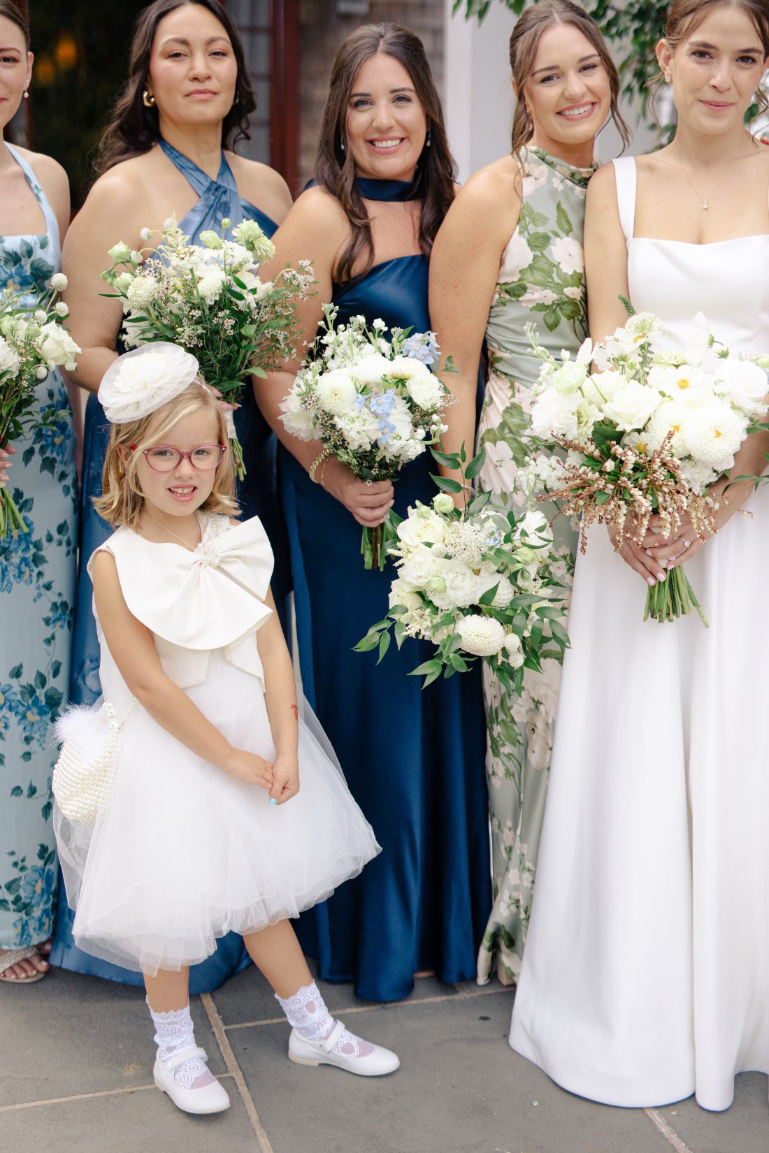 Bridesmaids in blue and green dresses with bride holding white floral bouquets outdoors