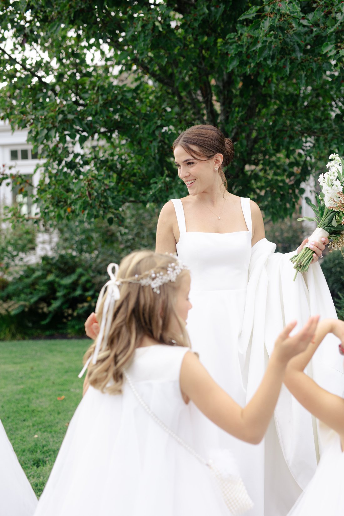Bride smiling with flower girls in white dresses during outdoor wedding portraits