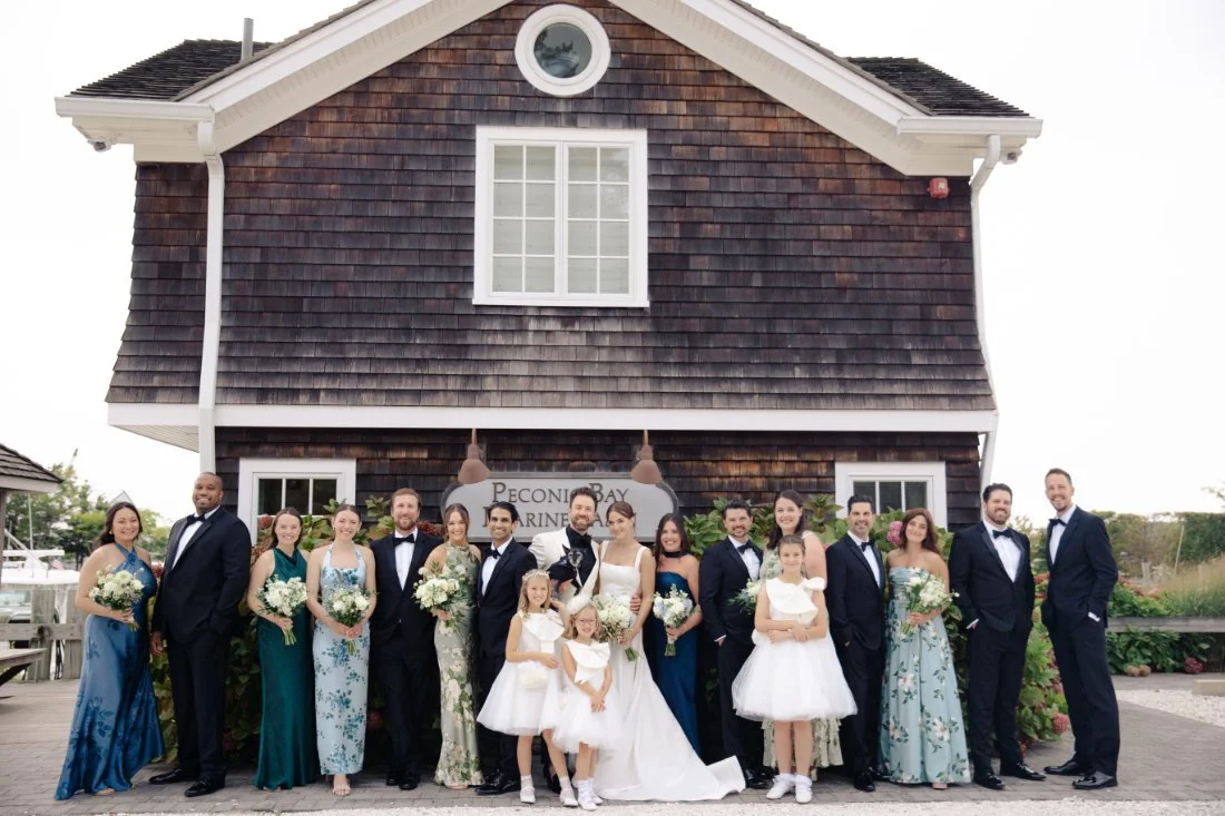 Full wedding party group portrait in front of Peconic Bay Yacht Club marina building