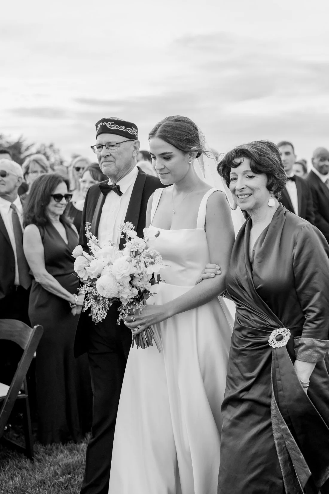 Black and white photo of bride walking down aisle with parents at Peconic Bay Yacht Club