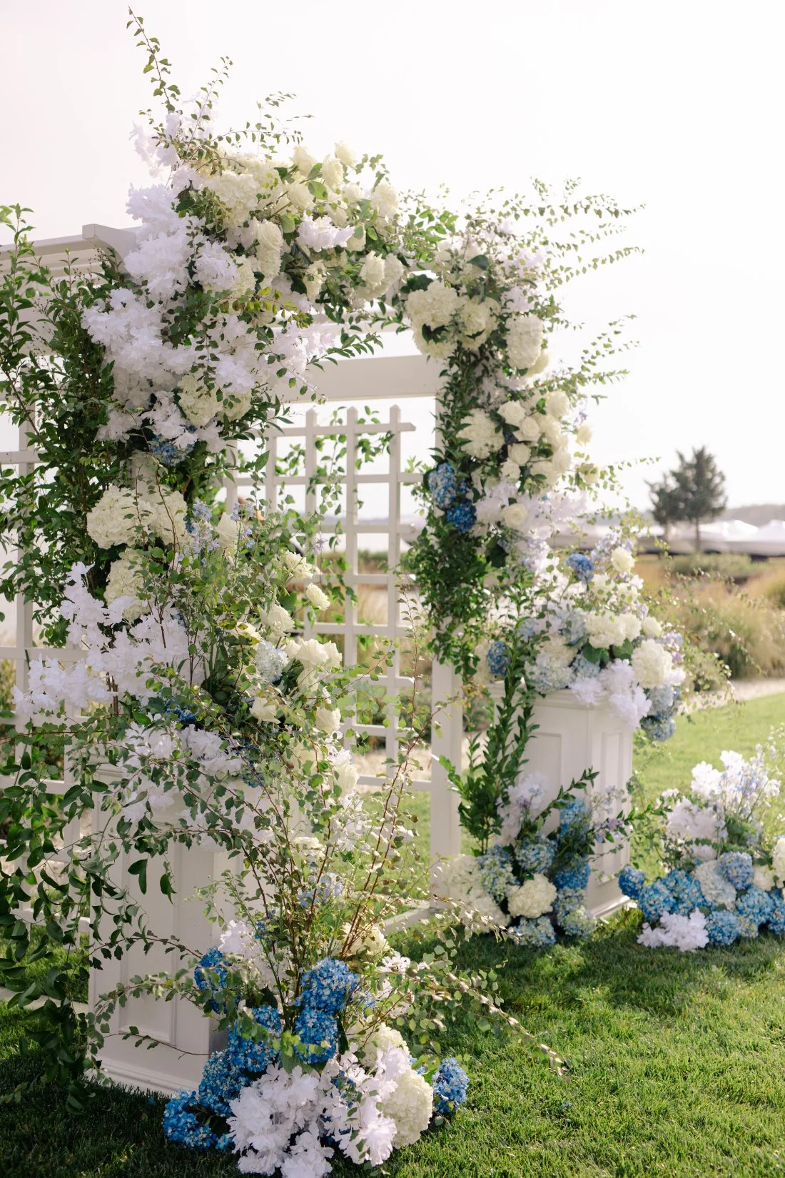 Close-up of white and blue floral ceremony arch with greenery by the waterfront