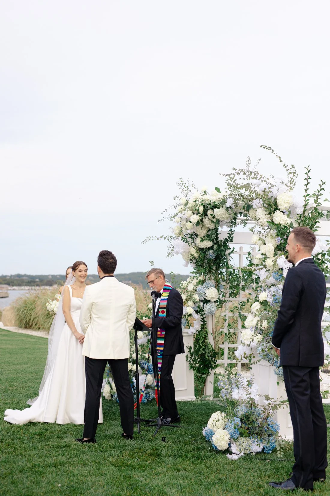 Bride and groom exchanging vows under floral arch at Peconic Bay Yacht Club