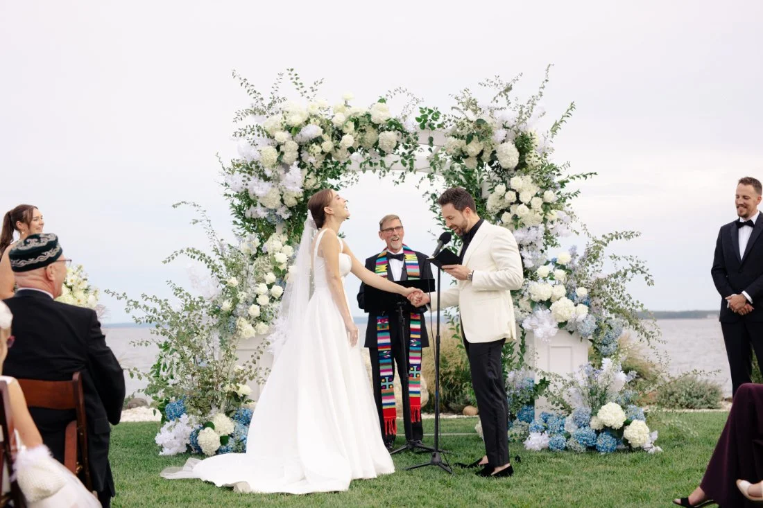 Couple holding hands and laughing during wedding ceremony by the water