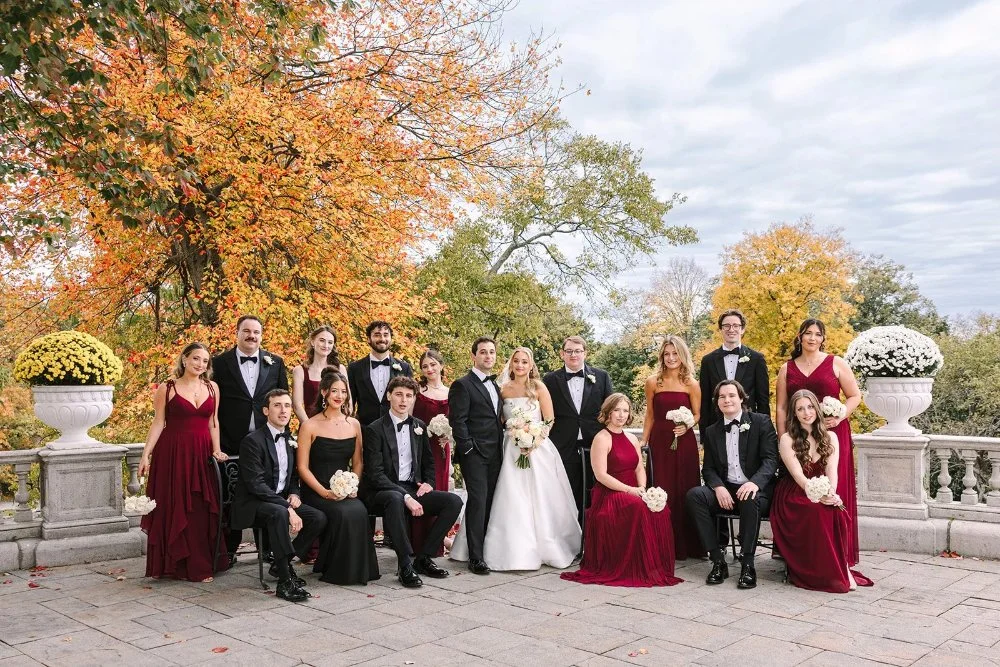 Wedding party in burgundy dresses and black tuxes posing outdoors with fall foliage in Tarrytown NY