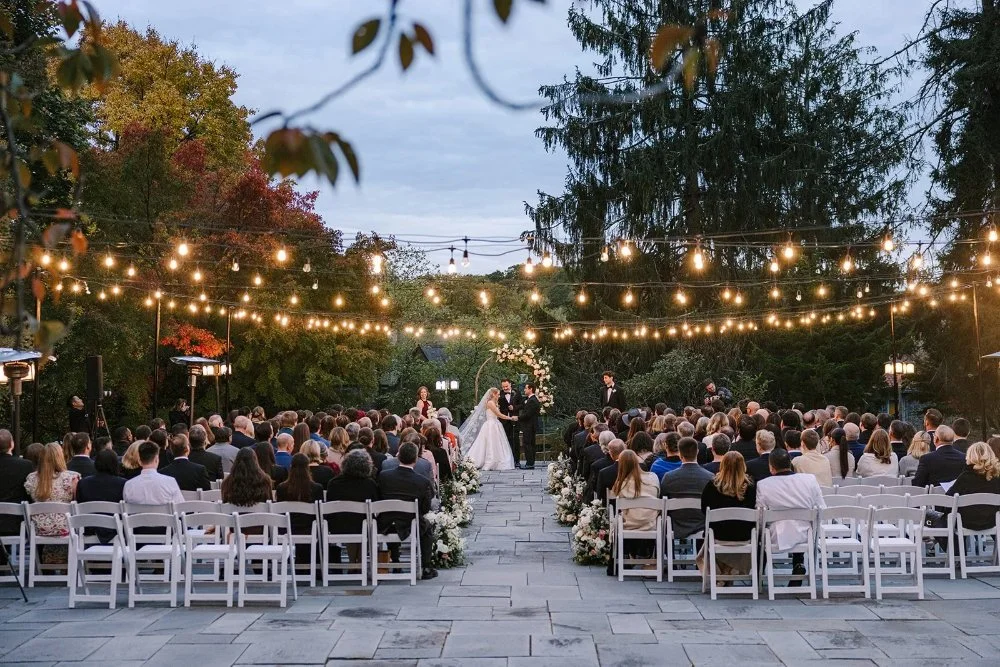 Wide shot of outdoor wedding ceremony with string lights at dusk in Tarrytown NY