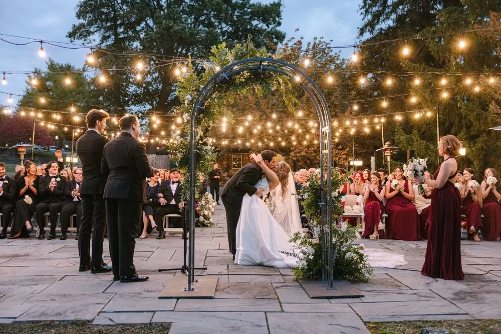 Bride and groom sharing their first kiss under floral arch at Tarrytown NY outdoor wedding