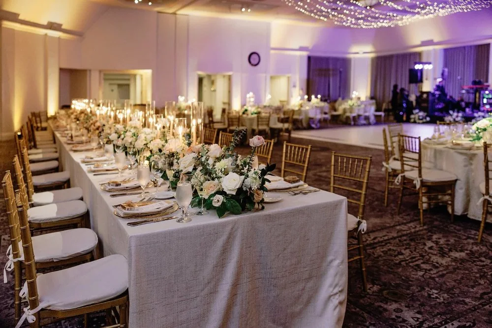 Reception space with long banquet tables, gold chairs, and soft candlelight ambiance