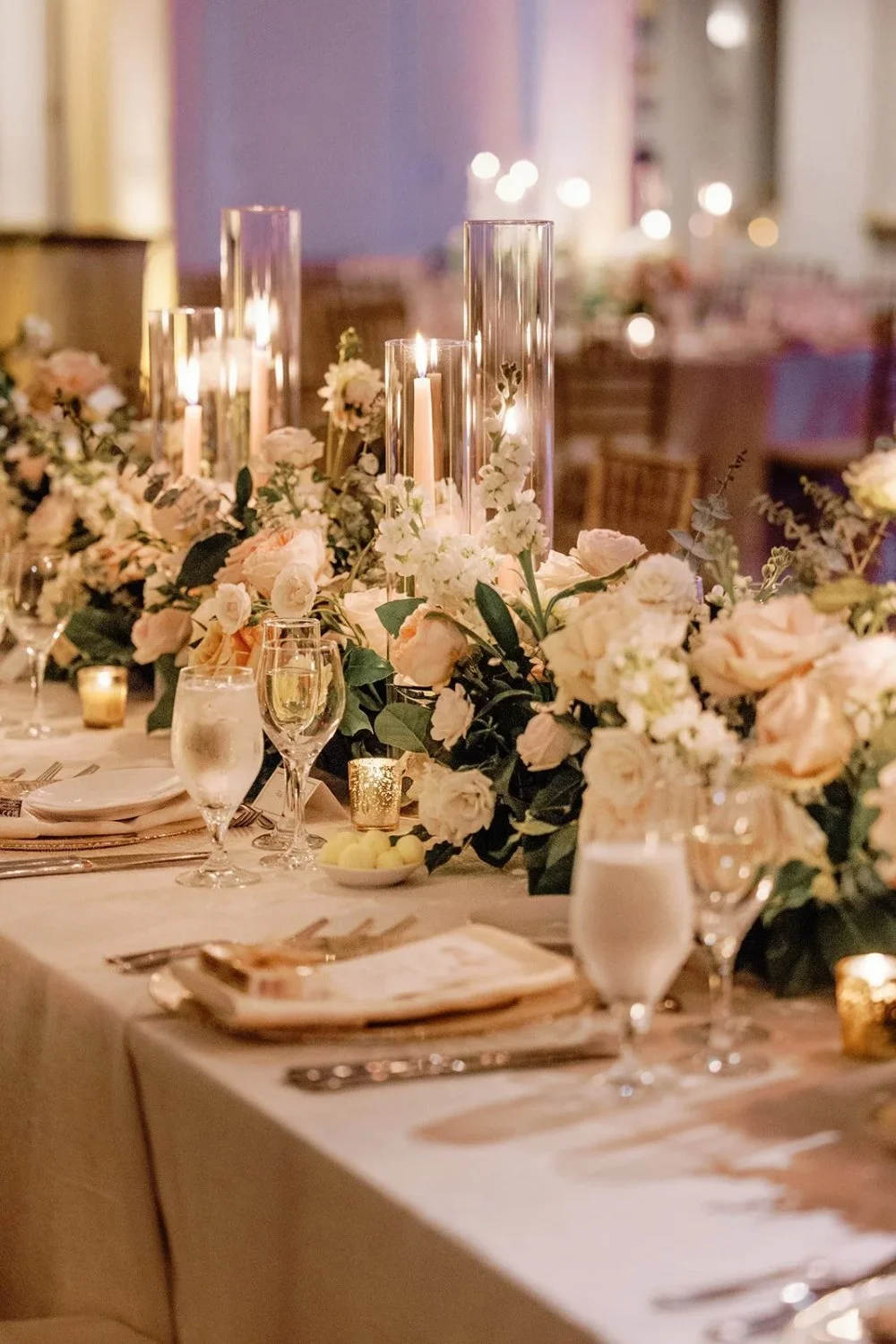 Tall glass candle centerpieces with lush floral arrangements on reception tables
