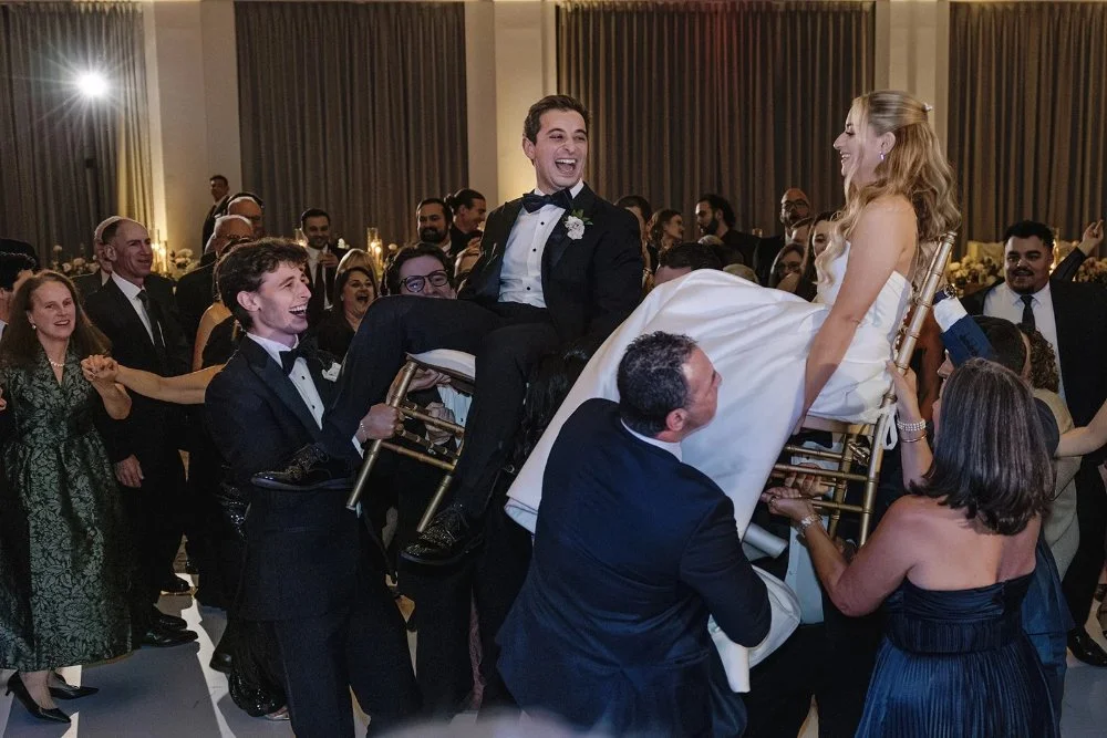Guests lifting bride and groom during lively hora dance celebration