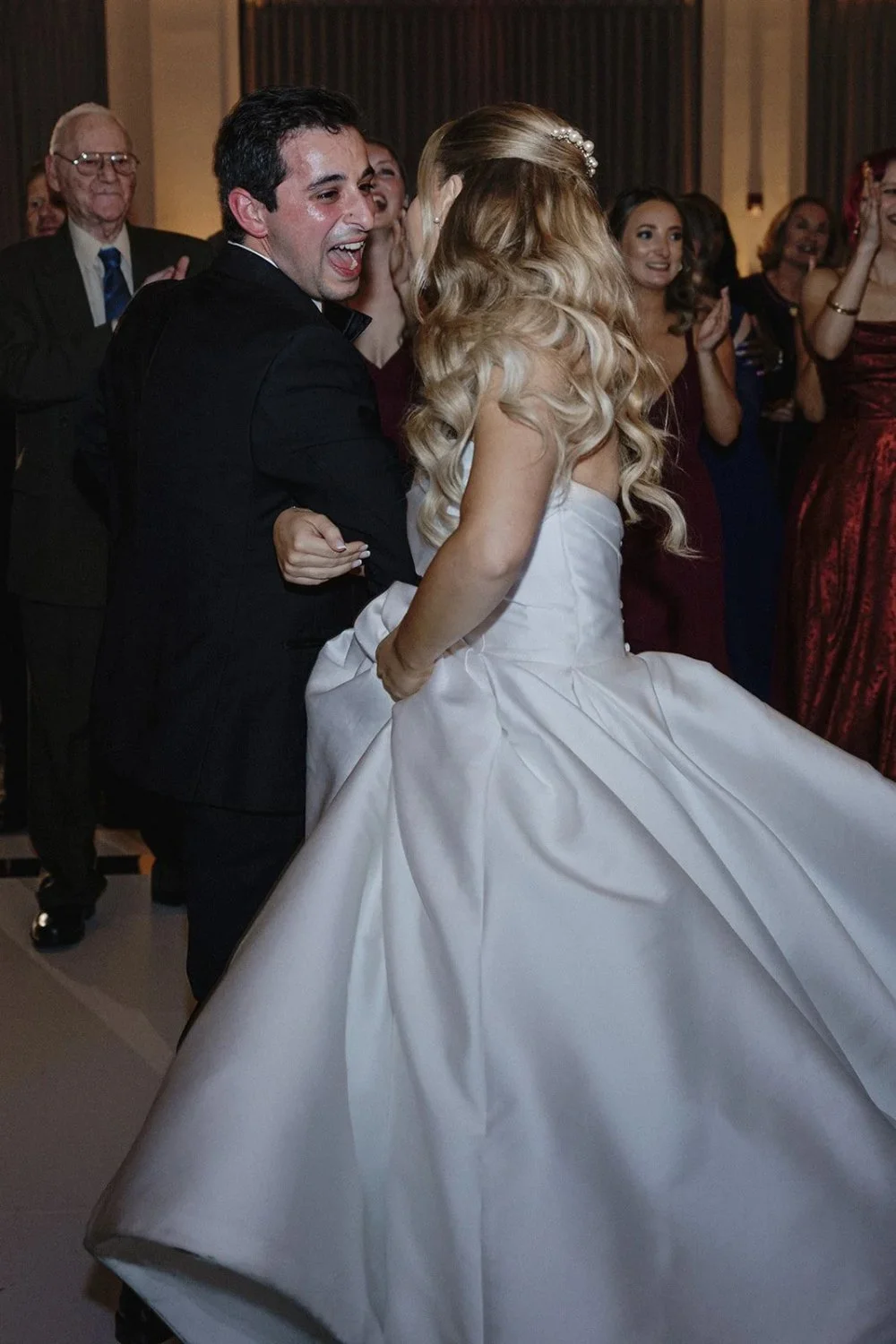 Bride and groom dancing together surrounded by cheering guests