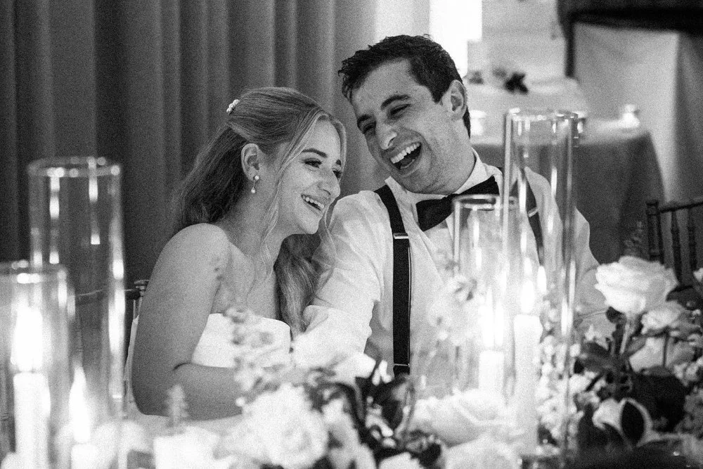 Couple laughing together at sweetheart table surrounded by candles and florals
