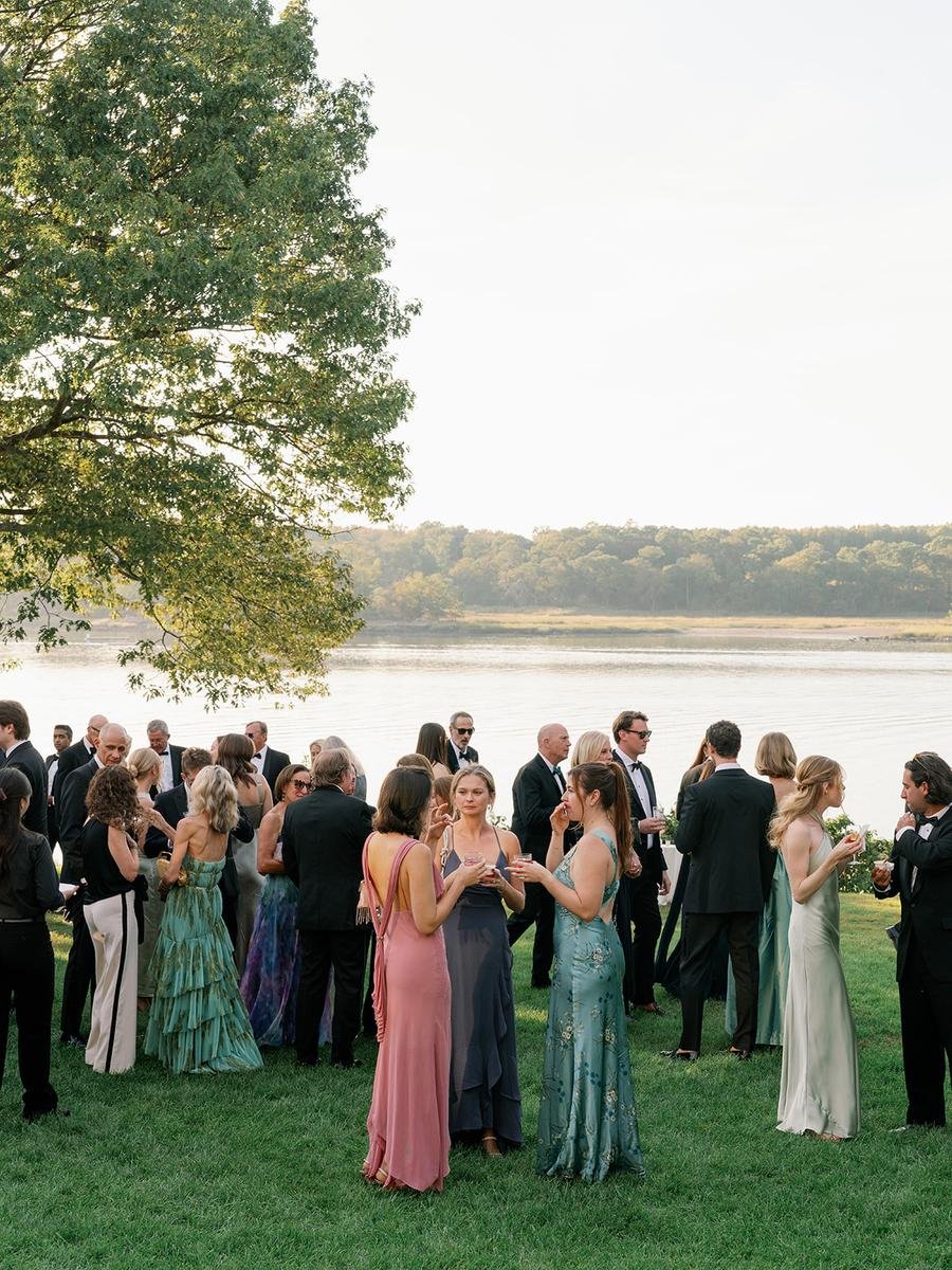 Wedding guests mingle on the waterfront lawn during cocktail hour with scenic views of the Long Island Sound in Rye, New York.