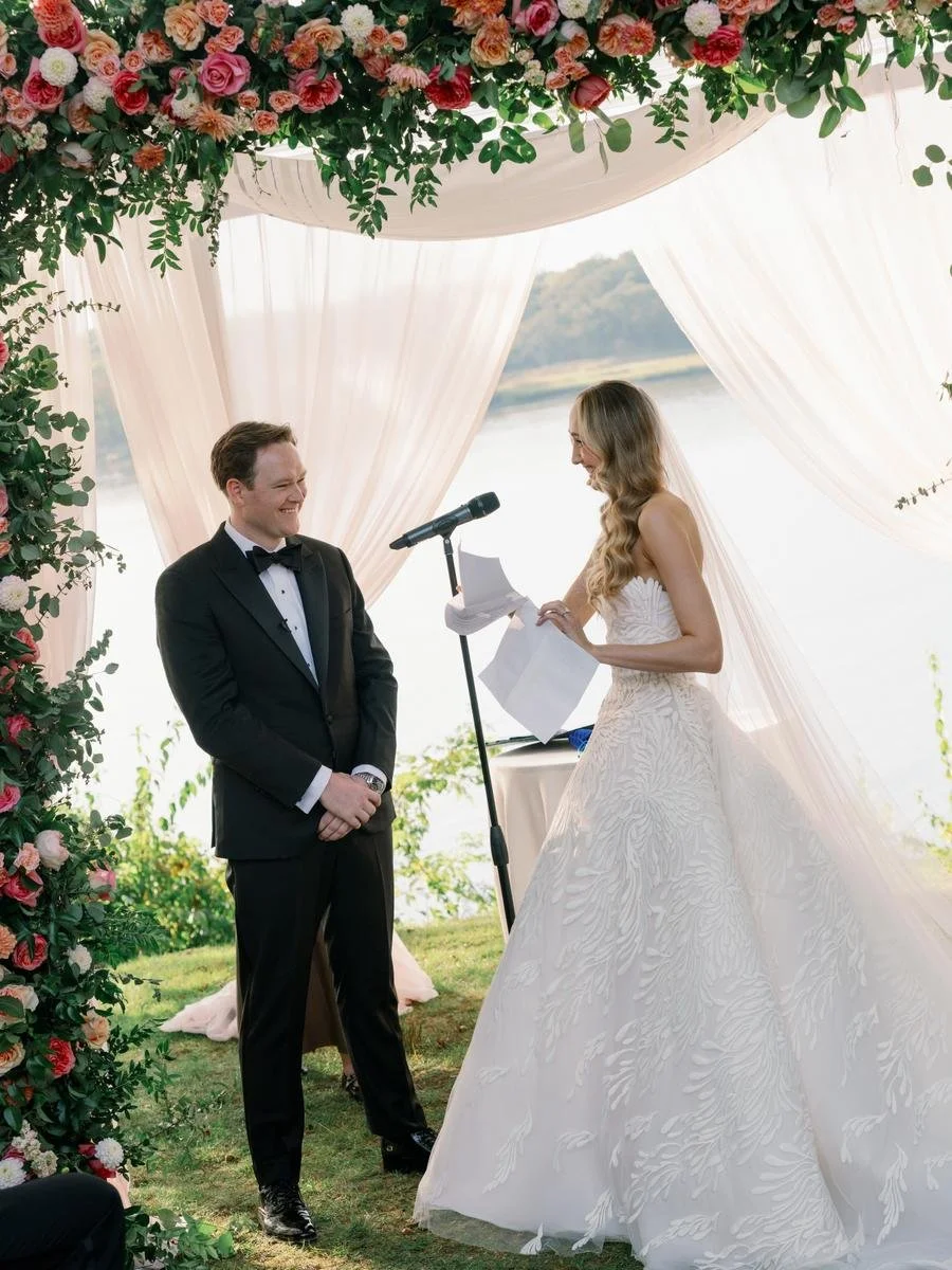 Bride listens to wedding vows beneath a floral chuppah overlooking the Long Island Sound during a Wainwright House wedding.