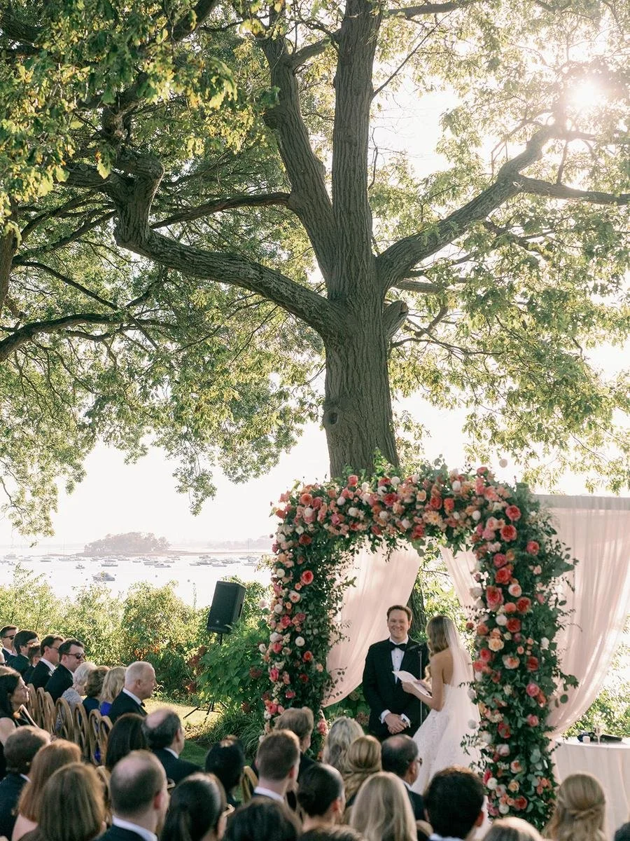 Couple kisses under a lush floral chuppah as guests applaud during an elegant Wainwright House wedding in Rye, New York.