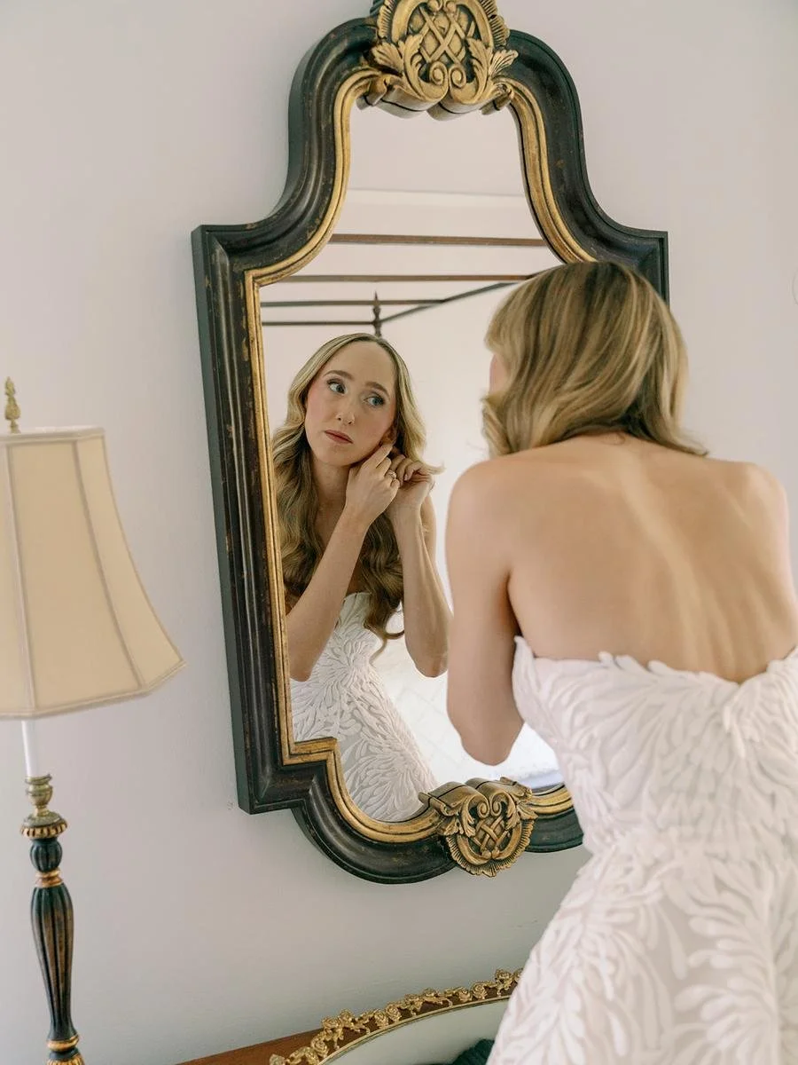 Bride puts on her earrings in an elegant mirror reflection before her Wainwright House wedding ceremony.