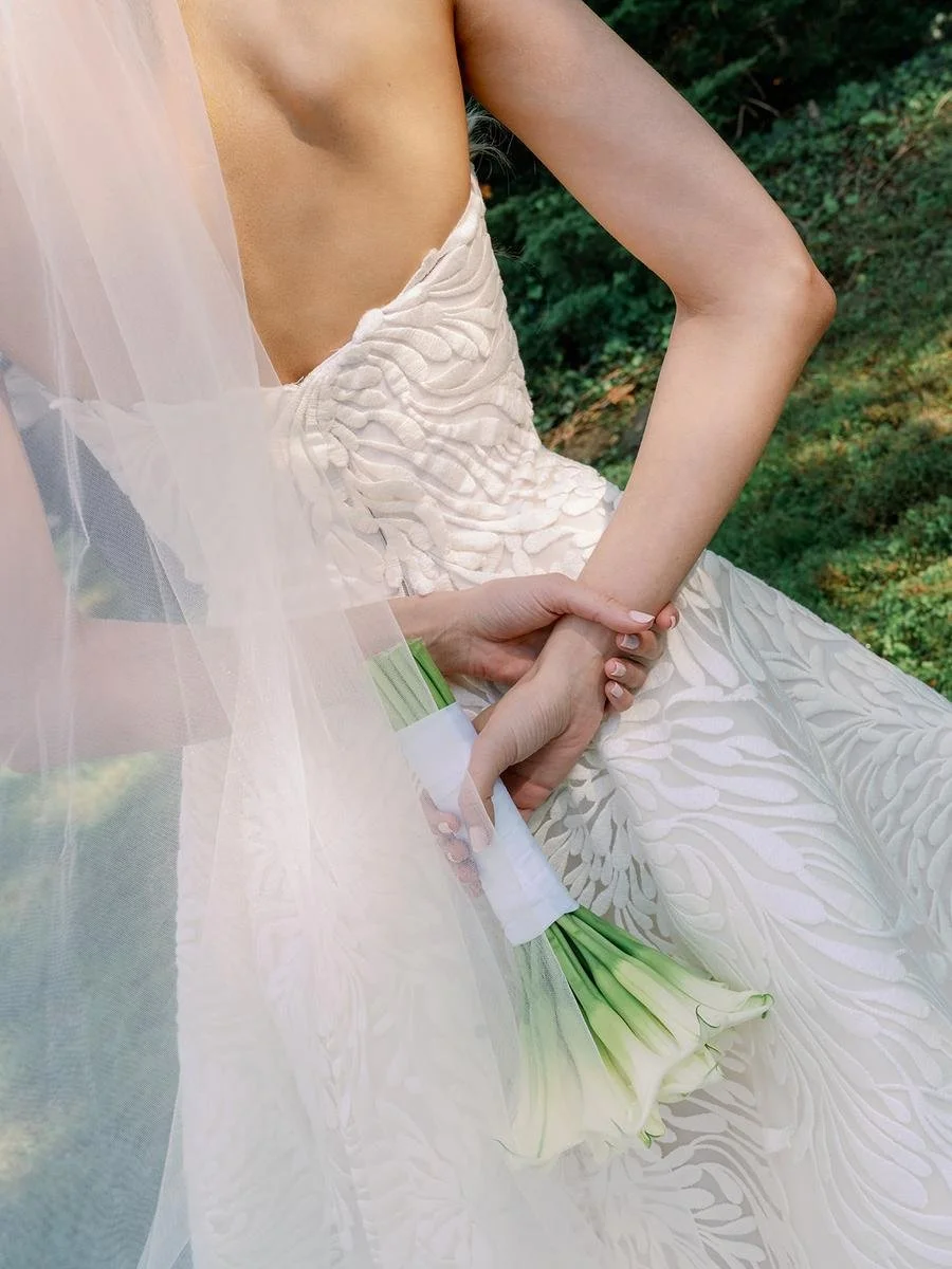 Close-up portrait of the bride holding a white calla lily bouquet behind her back.