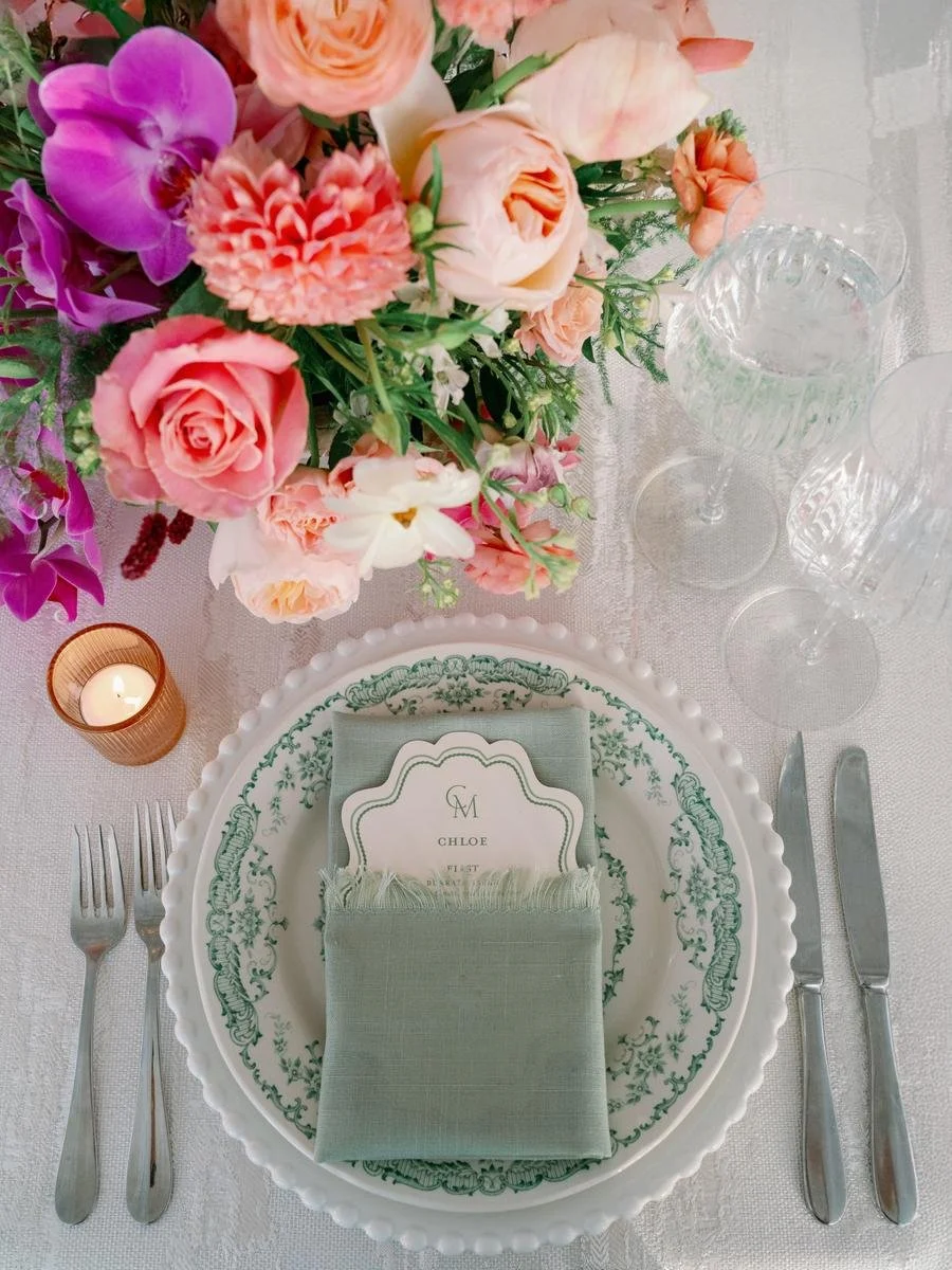 Elegant place setting with sage green linen napkin, vintage-inspired menu card, and floral centerpiece.