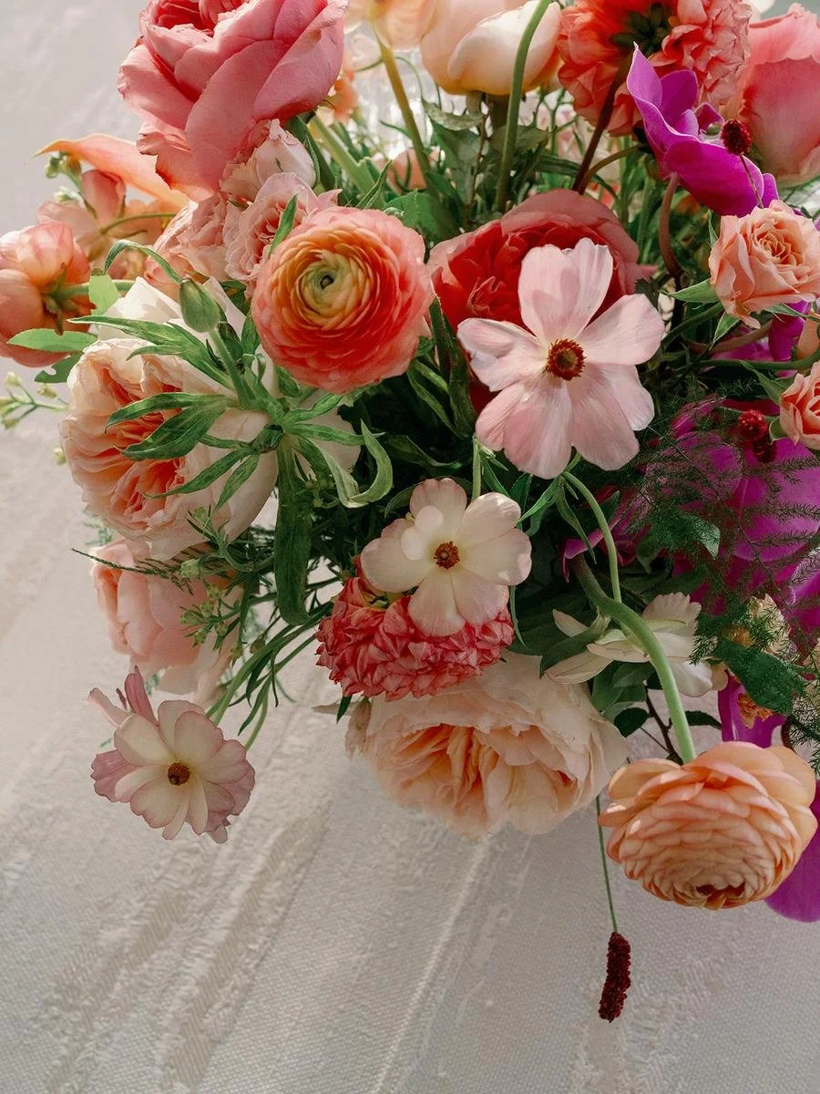 Close-up of a vibrant floral centerpiece with roses, orchids, ranunculus, and seasonal blooms.