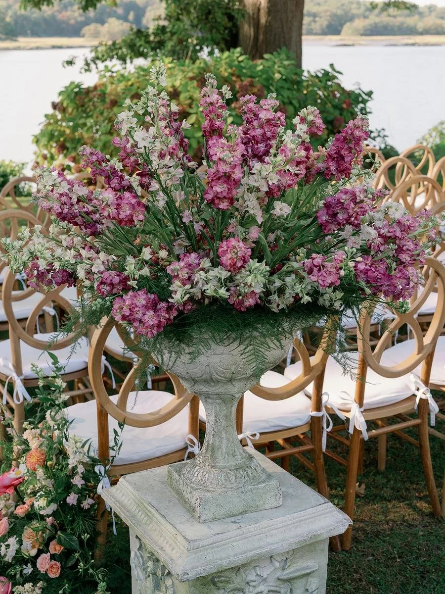 Tall floral urn arrangement framing the outdoor ceremony aisle beside the waterfront.