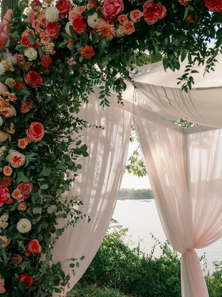 Floral ceremony arch draped in soft fabric overlooking the waterfront at a Wainwright House wedding.