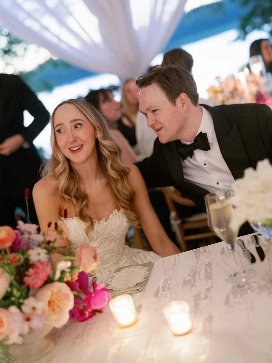 Bride and groom enjoying a quiet moment together at their reception table surrounded by floral arrangements.