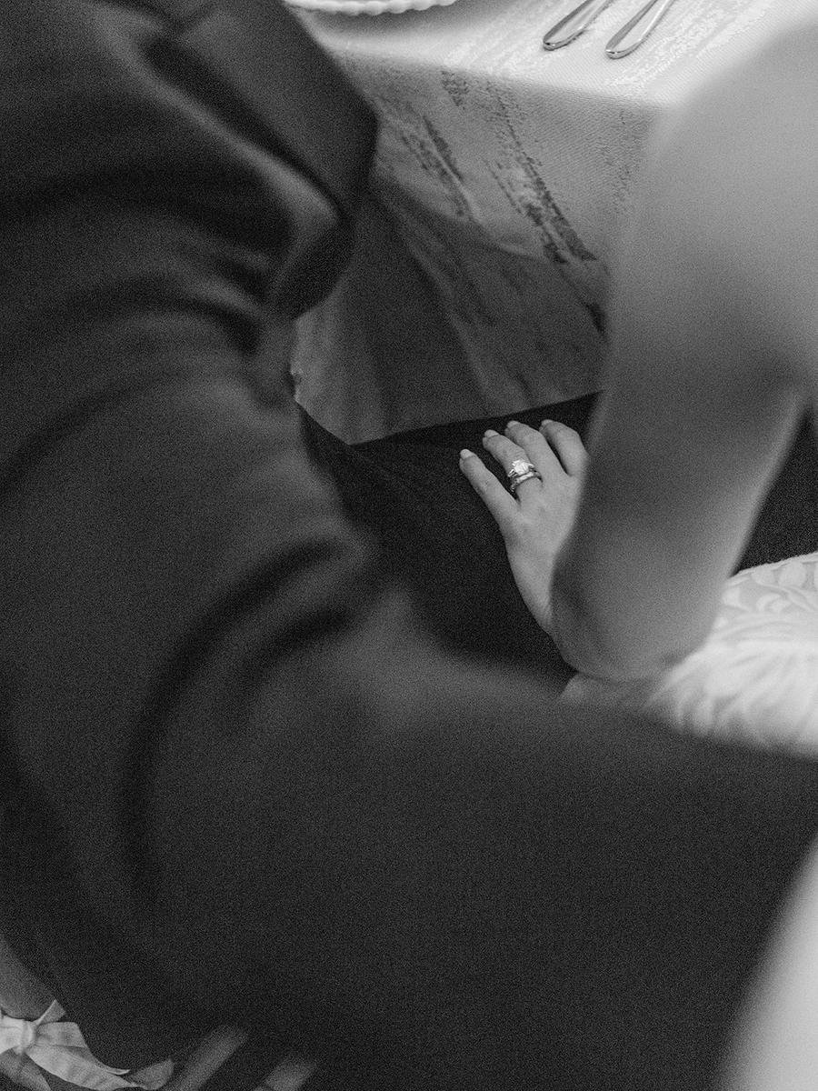 Close-up black-and-white detail of the bride’s wedding ring resting on the groom’s arm.