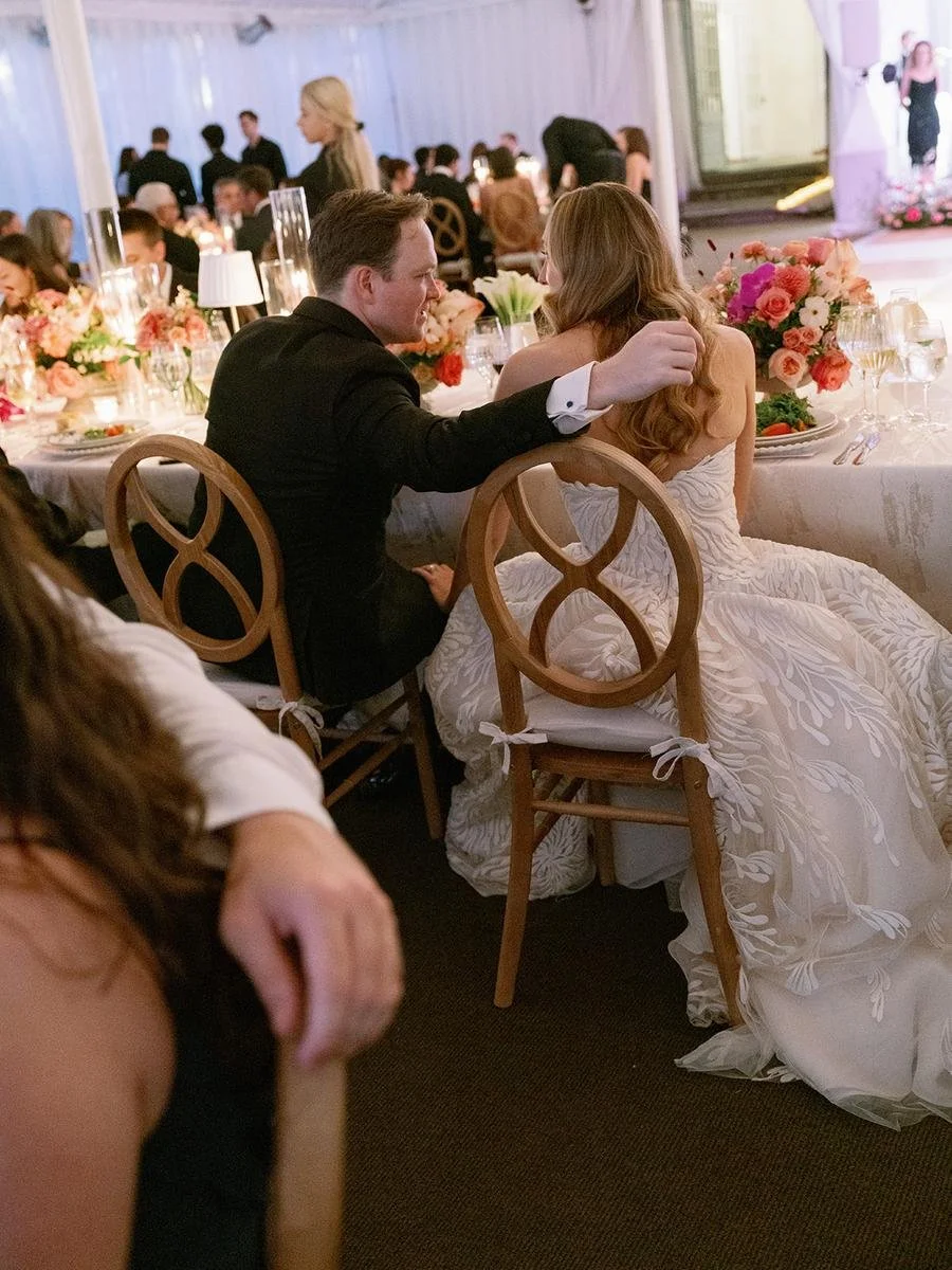 Newlyweds seated together at their sweetheart table surrounded by romantic floral centerpieces.