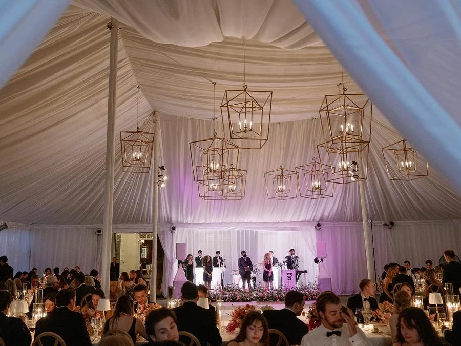 Wide view of the reception tent with a live band, candlelit tables, and geometric chandeliers at a Wainwright House wedding.