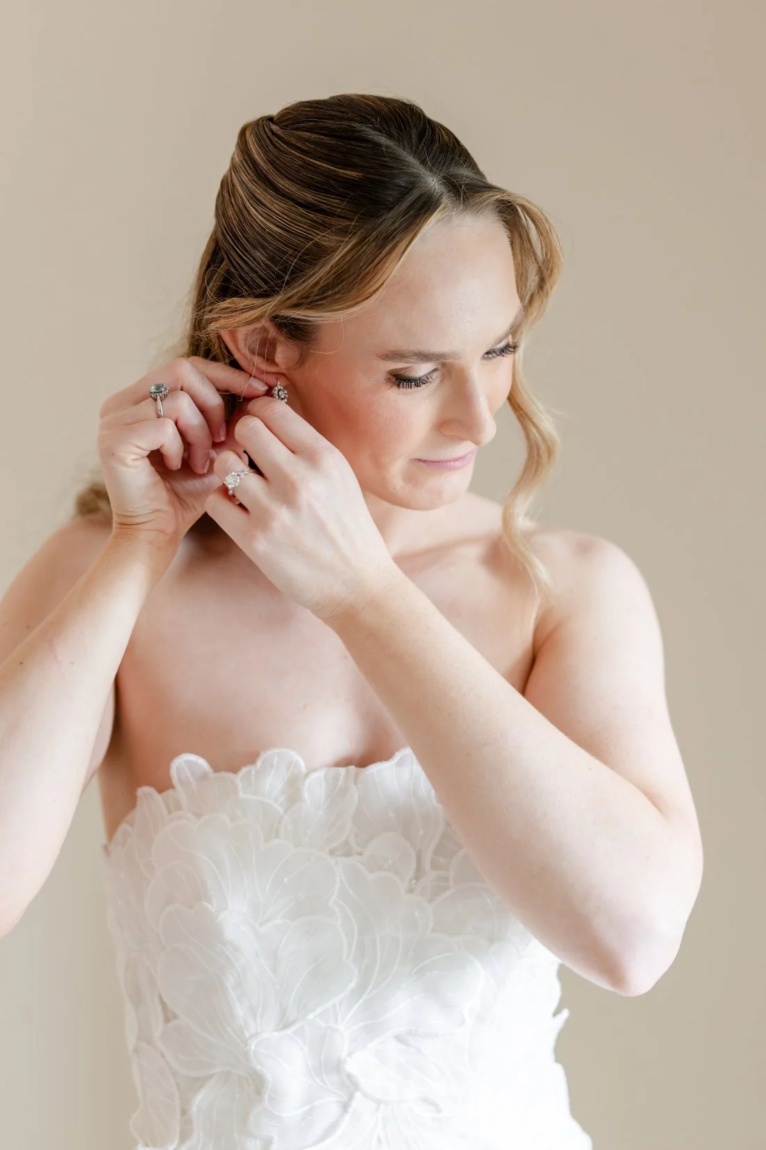 Bride putting on her earrings while wearing a strapless floral appliqué wedding gown