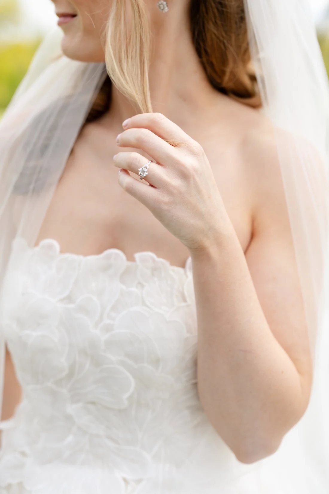Bride wearing a long veil and floral appliqué gown with her engagement ring