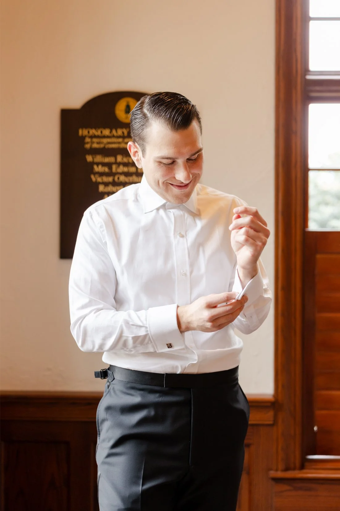 Groom getting ready in a white tuxedo shirt and fastening his cufflinks before his Quaker Ridge Golf Club wedding in New York.