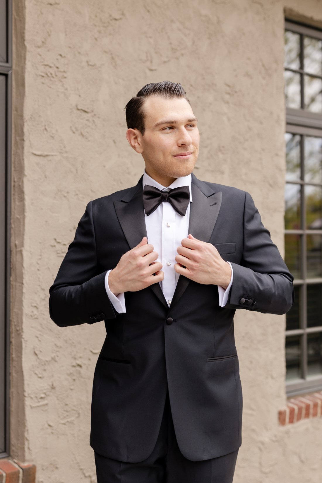 Groom dressed in a classic black tuxedo and bow tie posing outside before his Quaker Ridge Golf Club wedding in New York.