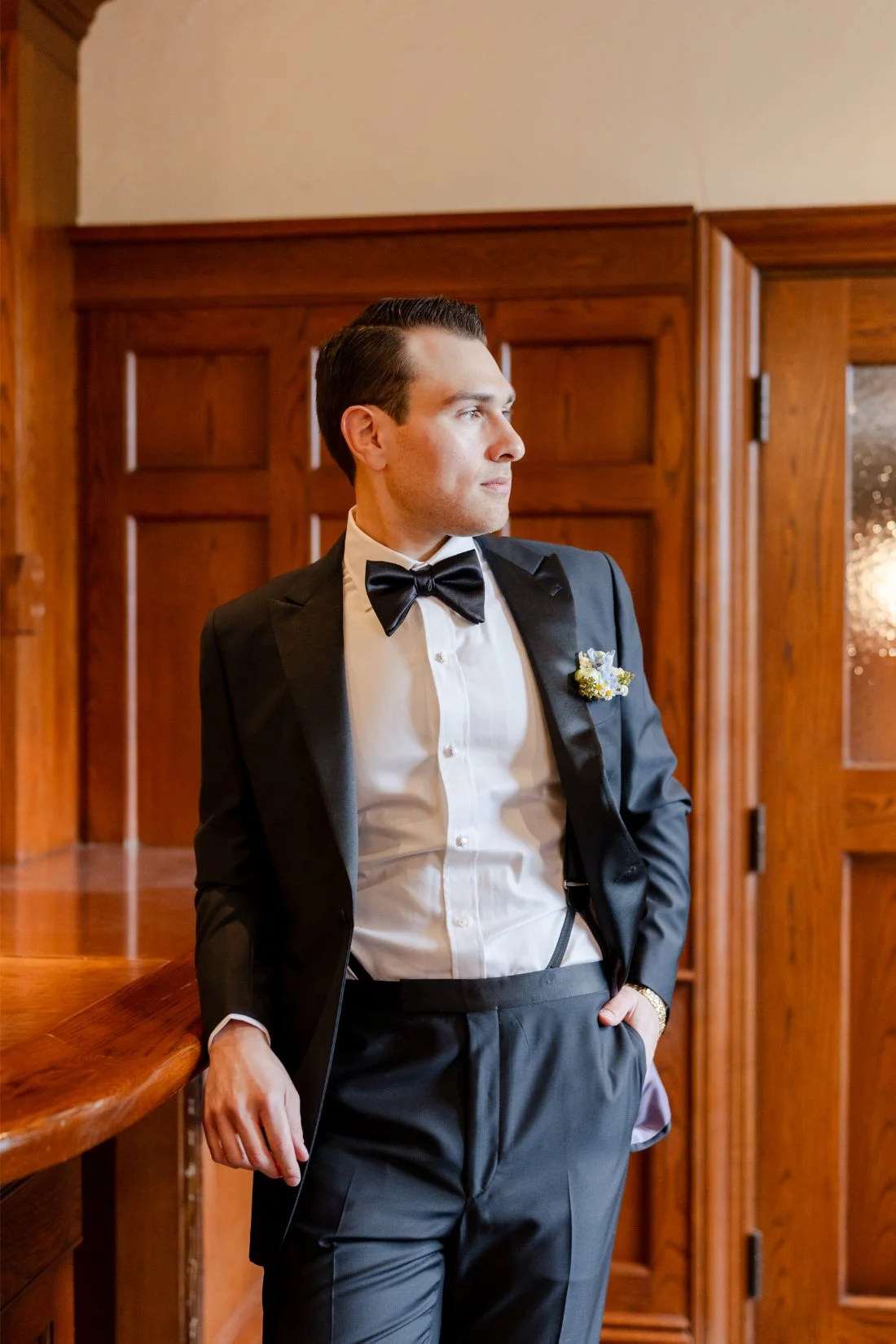 Groom in a black tuxedo and bow tie posing indoors during wedding portraits at Quaker Ridge Golf Club in New York.