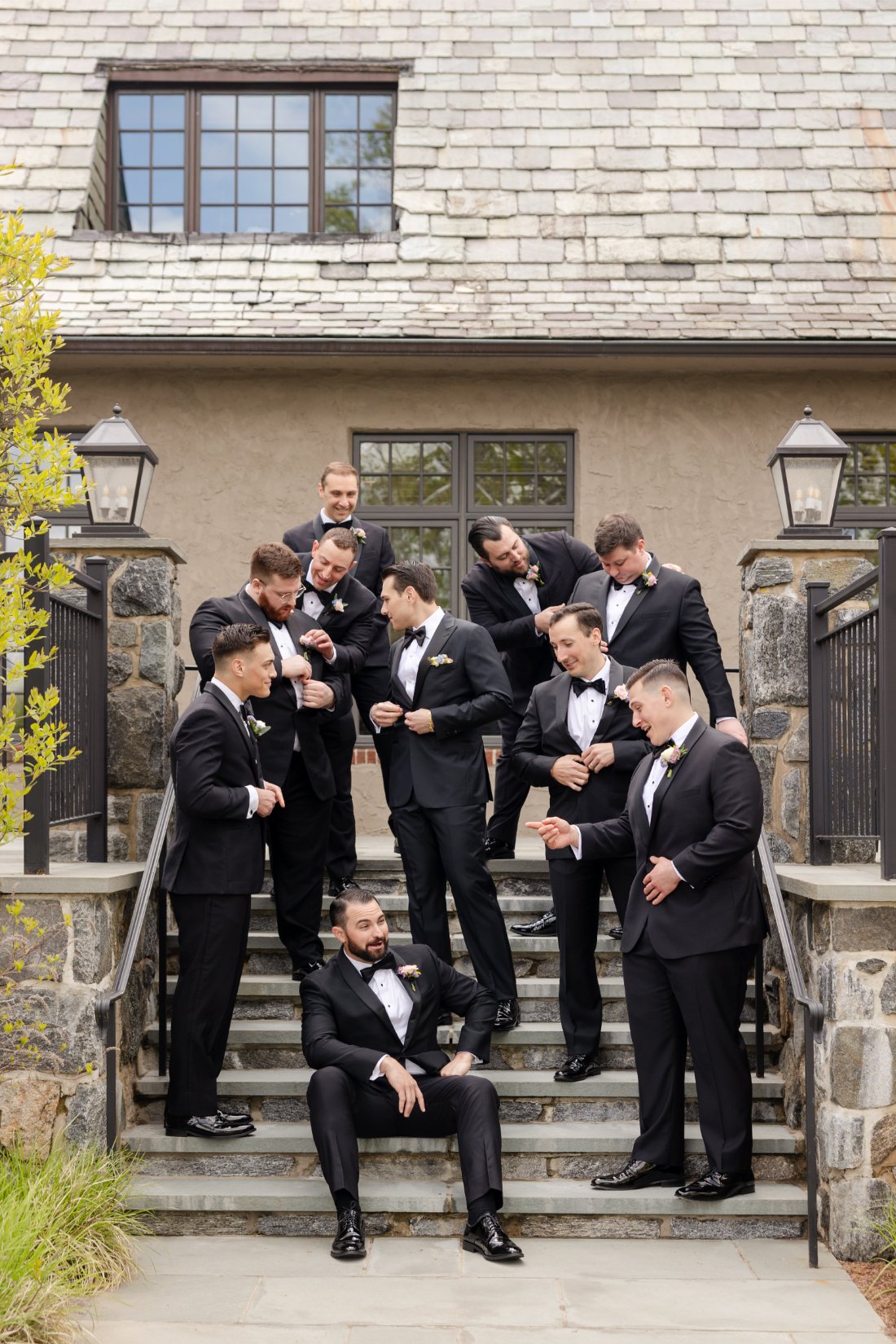 Groom and groomsmen in black tuxedos gathered on the outdoor steps for wedding party portraits at Quaker Ridge Golf Club.