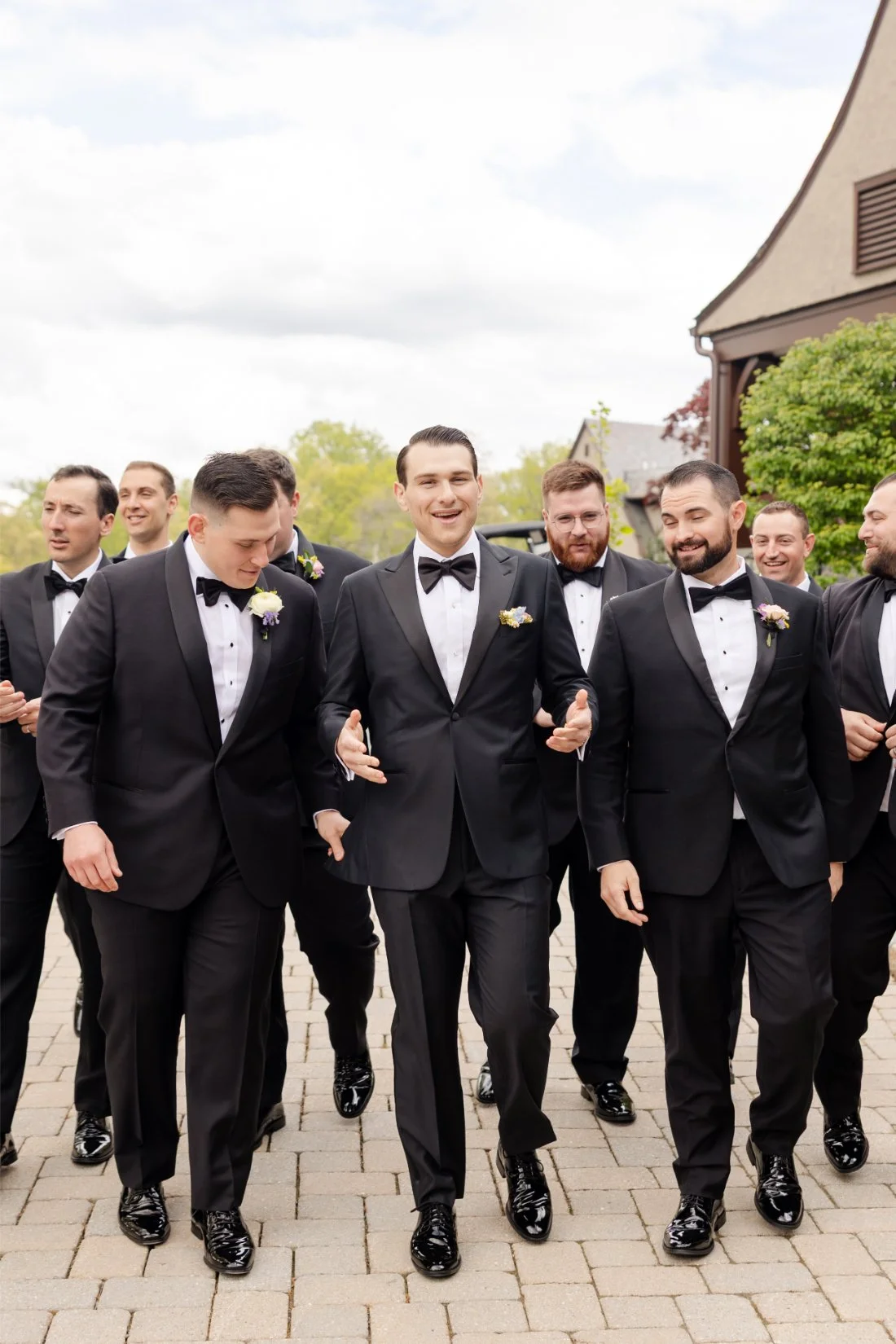 Groom walking outdoors with his groomsmen in black tuxedos before the wedding ceremony at Quaker Ridge Golf Club in New York.