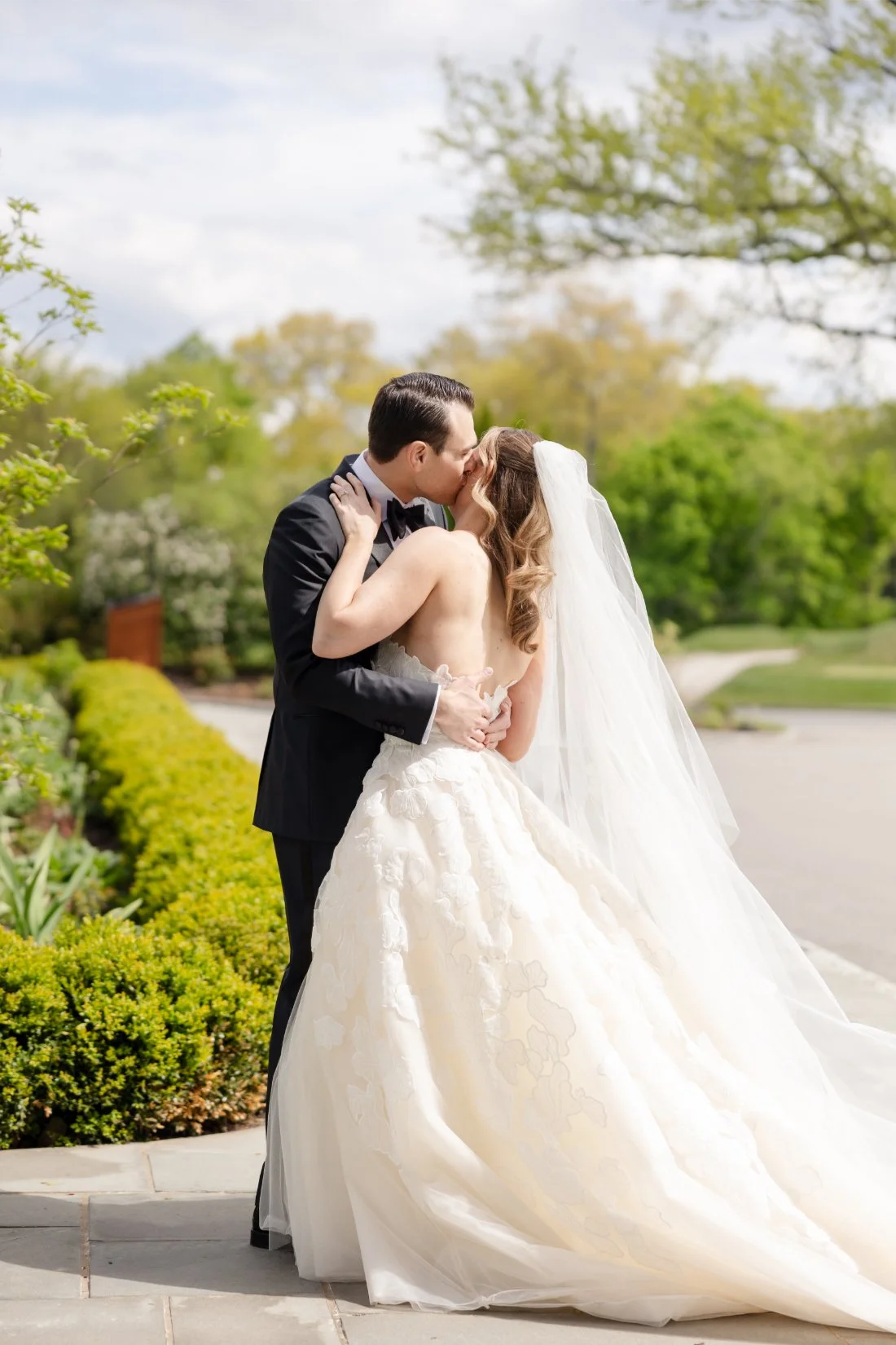 Bride and groom share a kiss surrounded by lush spring greenery