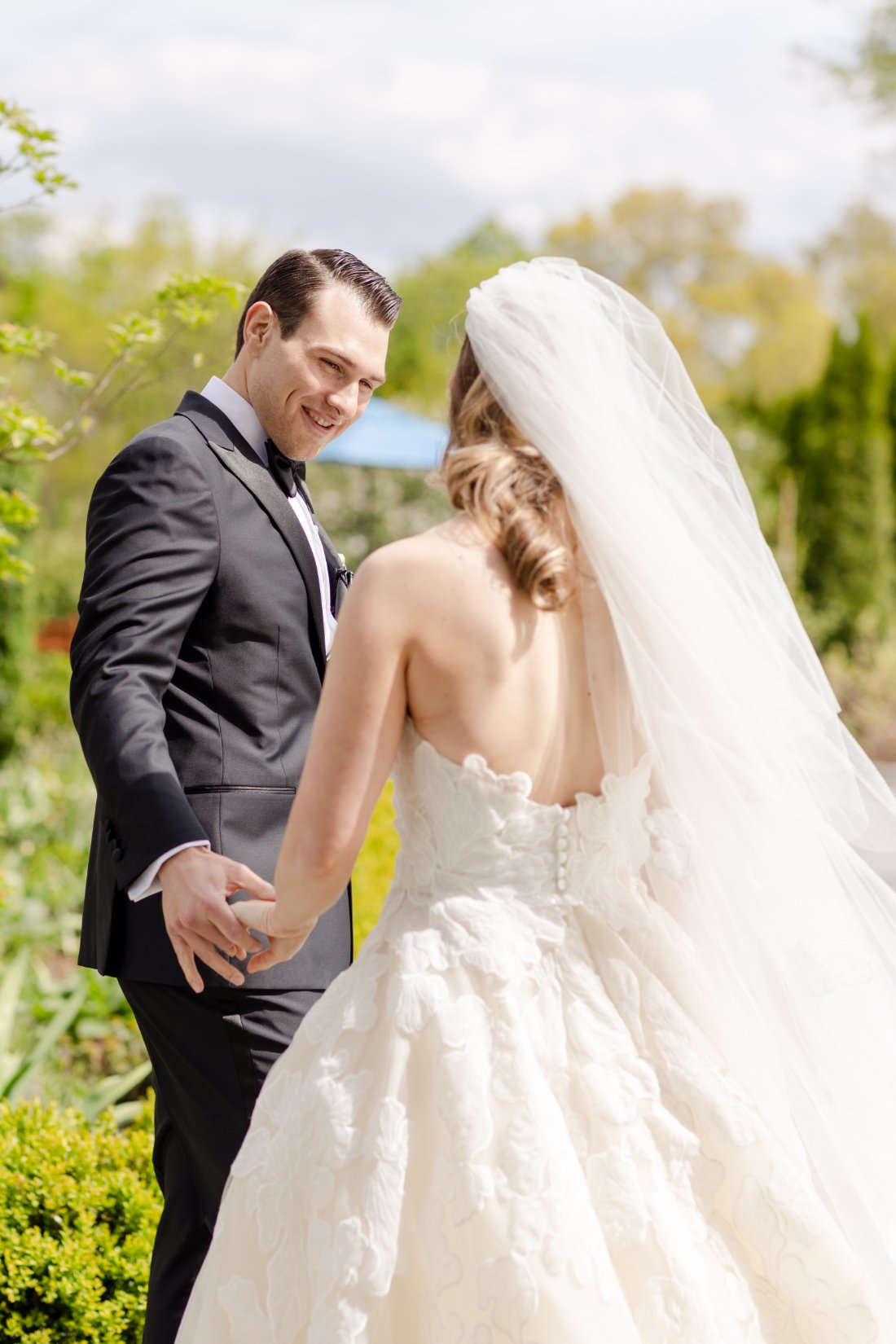 Groom smiles at his bride as they hold hands during outdoor wedding portraits