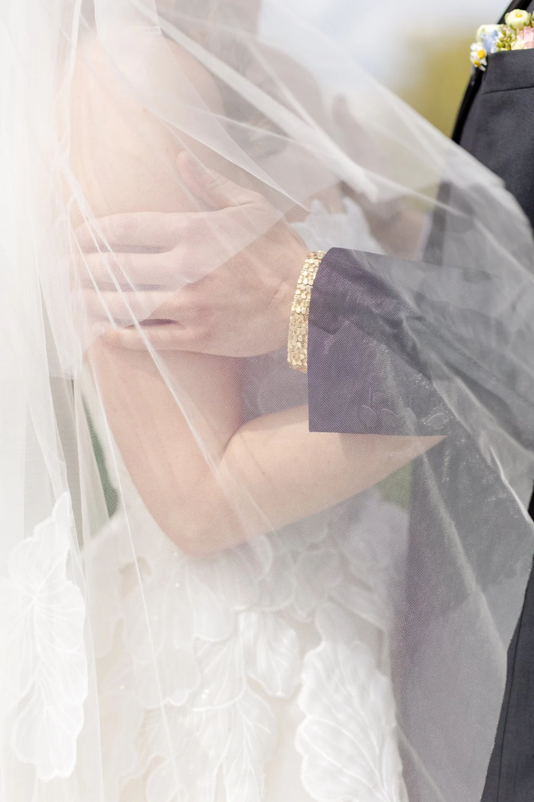 Close-up of bride and groom holding hands beneath her sheer wedding veil