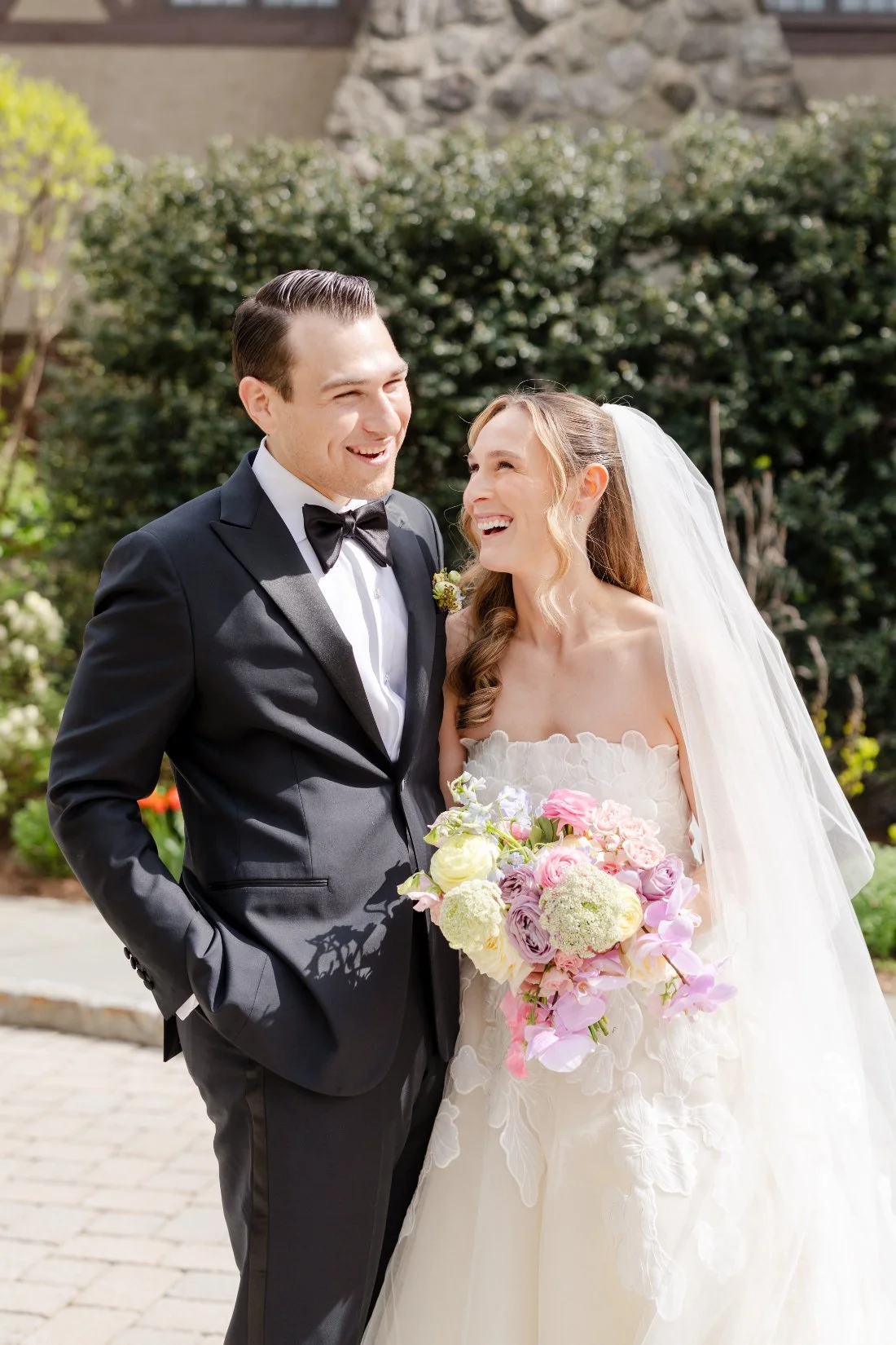 Bride and groom laugh together while posing with a colorful spring bouquet