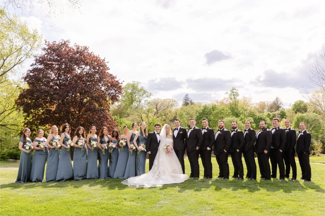 Bride and groom pose with their full wedding party outdoors at a Quaker Ridge Golf Club wedding