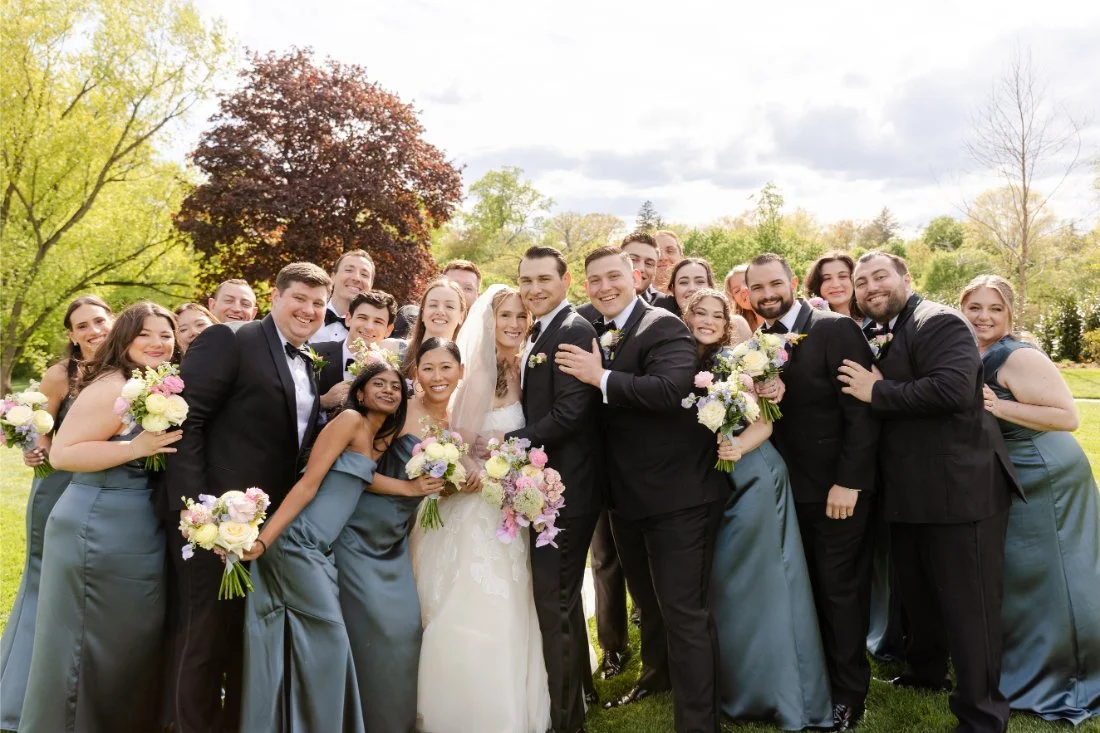 Bride and groom laugh with bridesmaids and groomsmen during joyful wedding party portraits