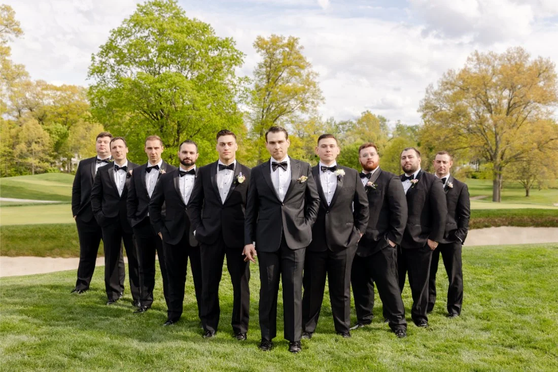 Groom and groomsmen pose in black tuxedos on the green at Quaker Ridge Golf Club wedding