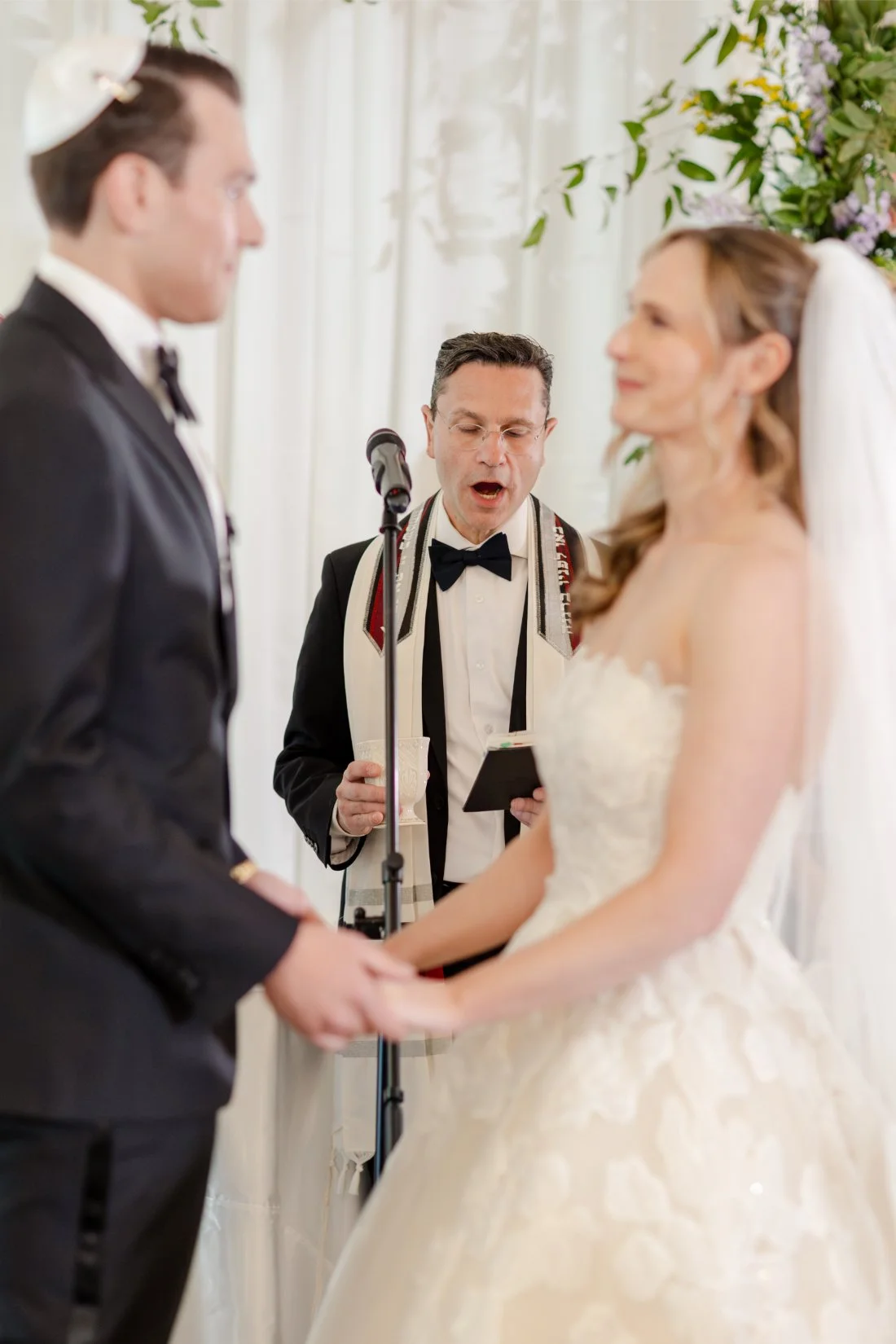 Bride and groom holding hands during their Jewish wedding ceremony.