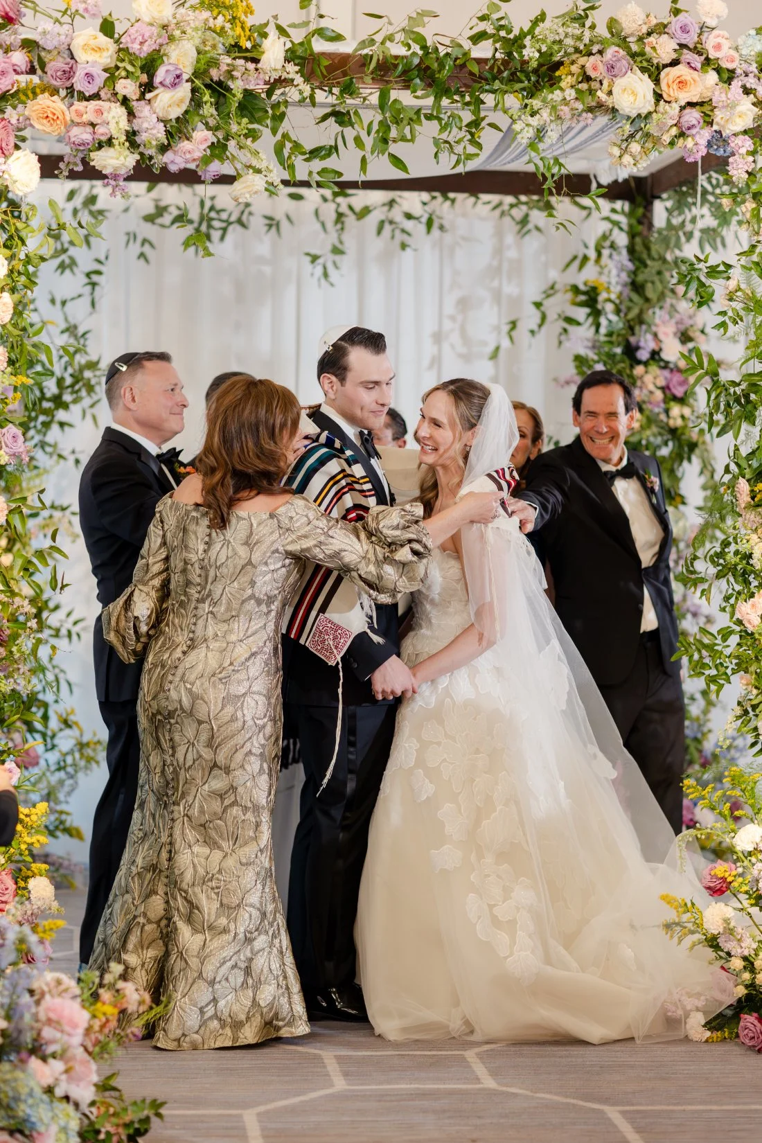 Parent placing a traditional Jewish prayer shawl over the groom’s shoulders during the ceremony.