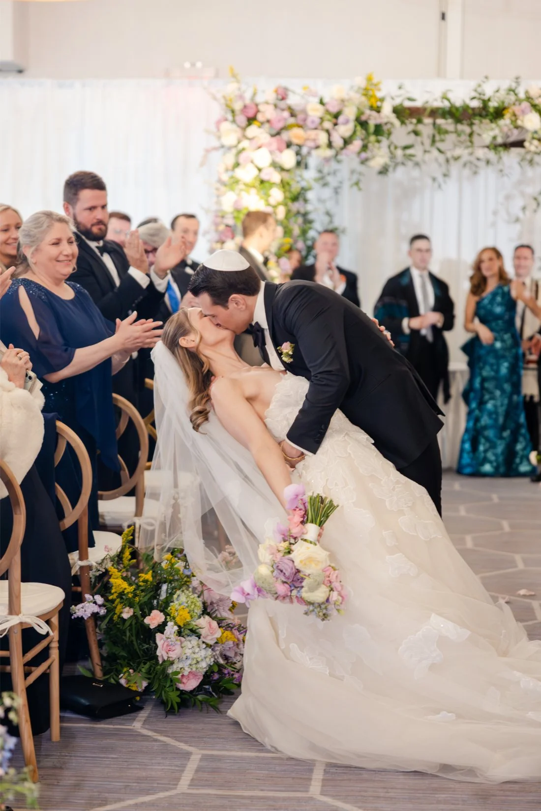 Newlyweds sharing a celebratory dip kiss at the end of the wedding aisle.