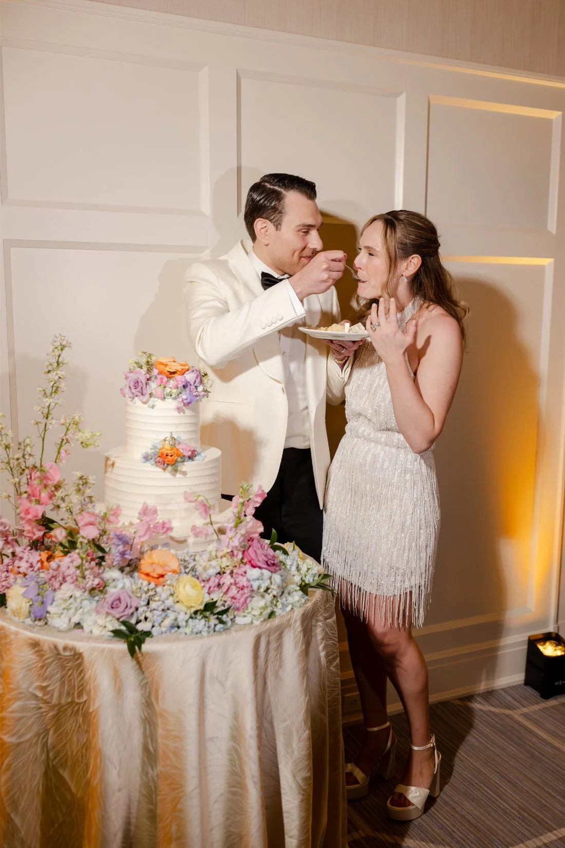 Newlyweds smiling as they cut the cake at their Quaker Ridge Golf Club wedding reception.