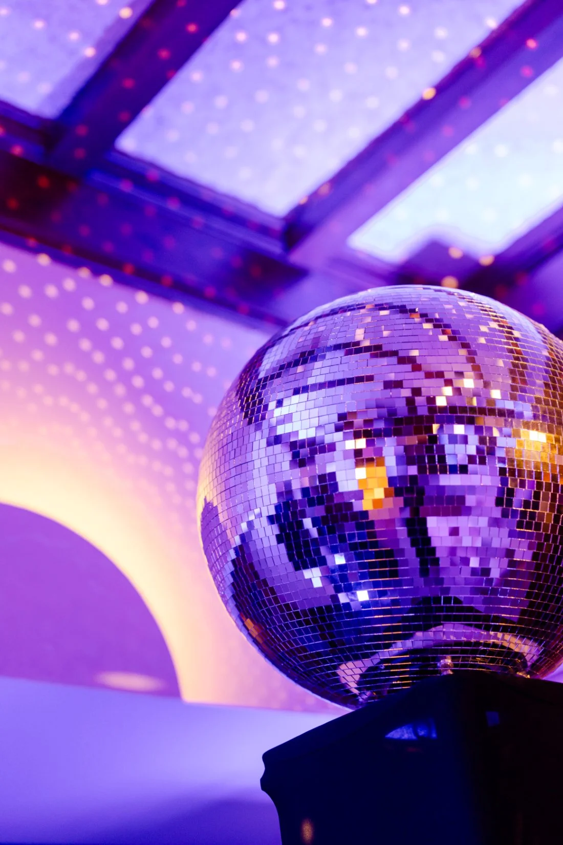 Disco ball reflecting purple and pink lighting across the wedding reception.