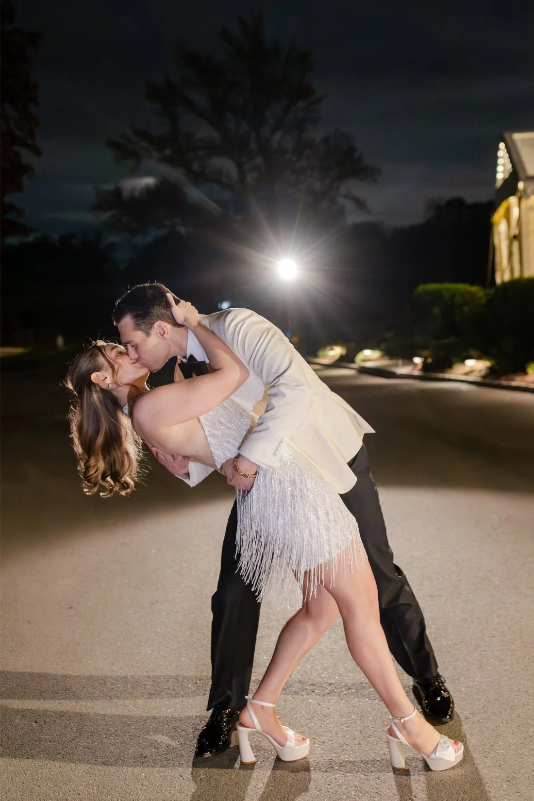Bride and groom sharing a romantic dipped kiss during their nighttime wedding portraits.