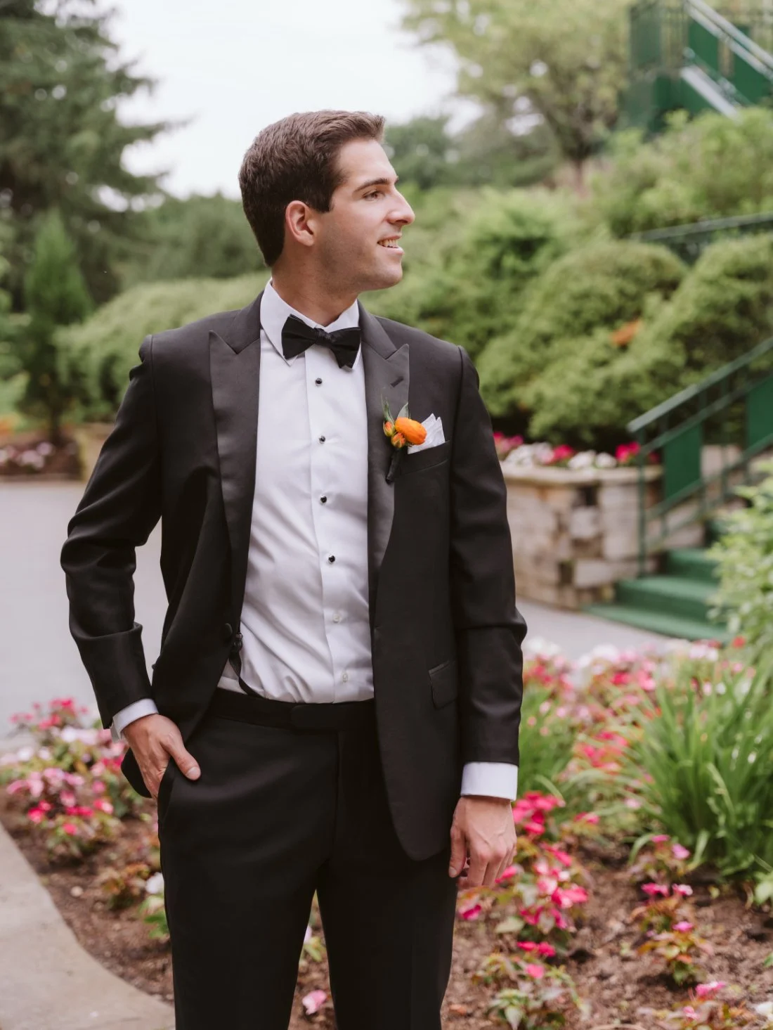 Groom wearing a classic black tuxedo and orange rose boutonniere outside during his Tappan Hill Mansion wedding.