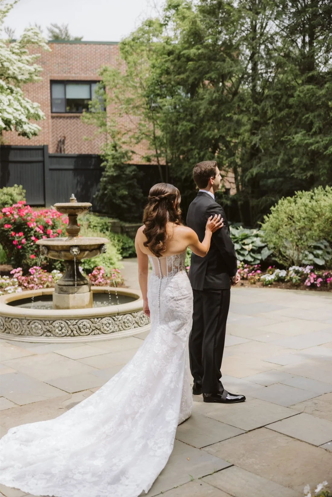 Sydney taps Matt on the shoulder during their Tappan Hill Mansion wedding first look beside a stone fountain and blooming garden.